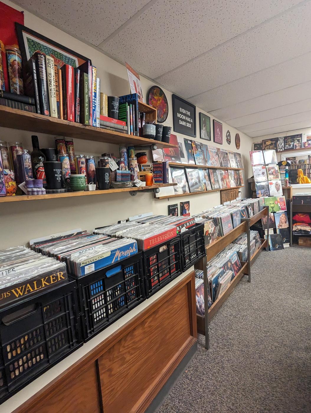 Inside FM Music: crates on the counter labelled Punk/Garage, Rap and Reggae, wall rails of displayed sleeves, and shelves of music books and candles.
